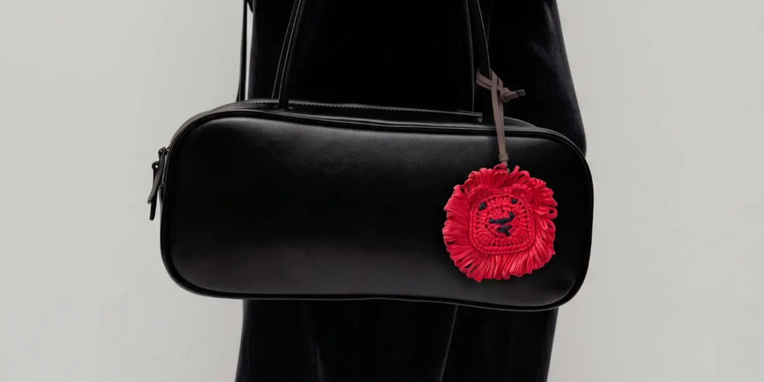 a red lion raffia charm tied to a black tote leather bag