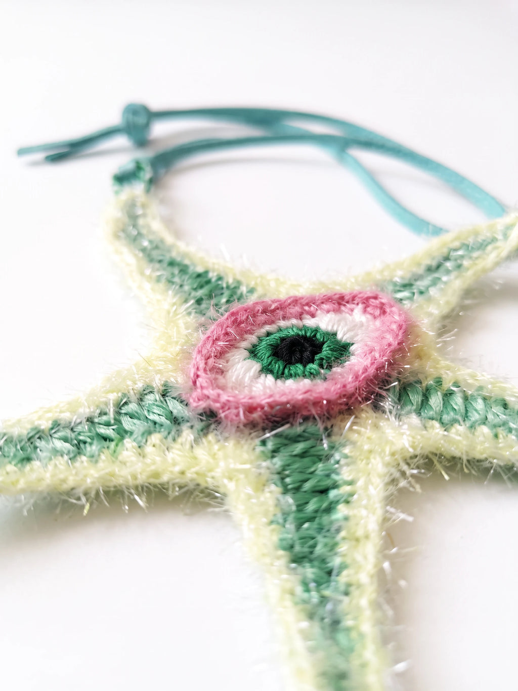 A close-up of a raffia starfish charm with five green and pale yellow arms and evil eye