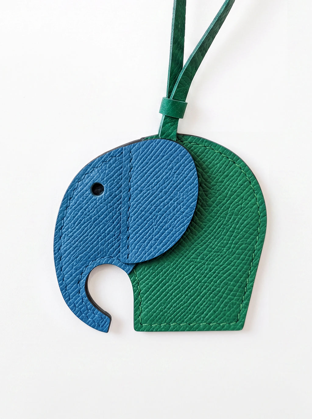 A two-tone elephant-shaped leather luggage tag or keychain charm in blue and green, featuring a textured grain finish and a matching green strap, shown on a plain white background.