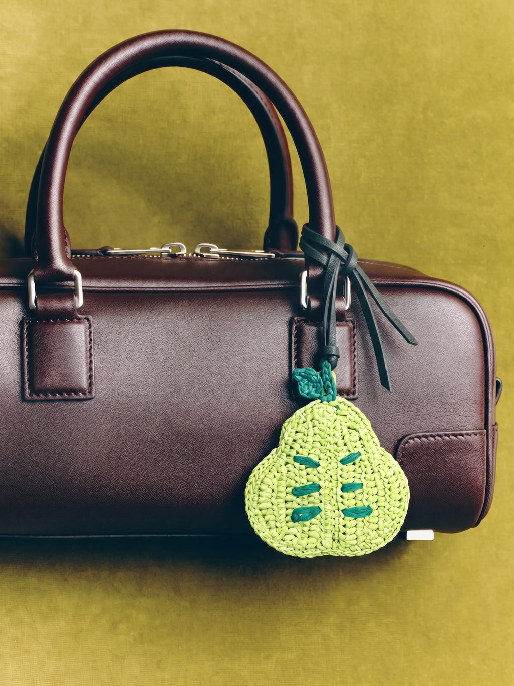 a green pear charm on a dark brown leather bag