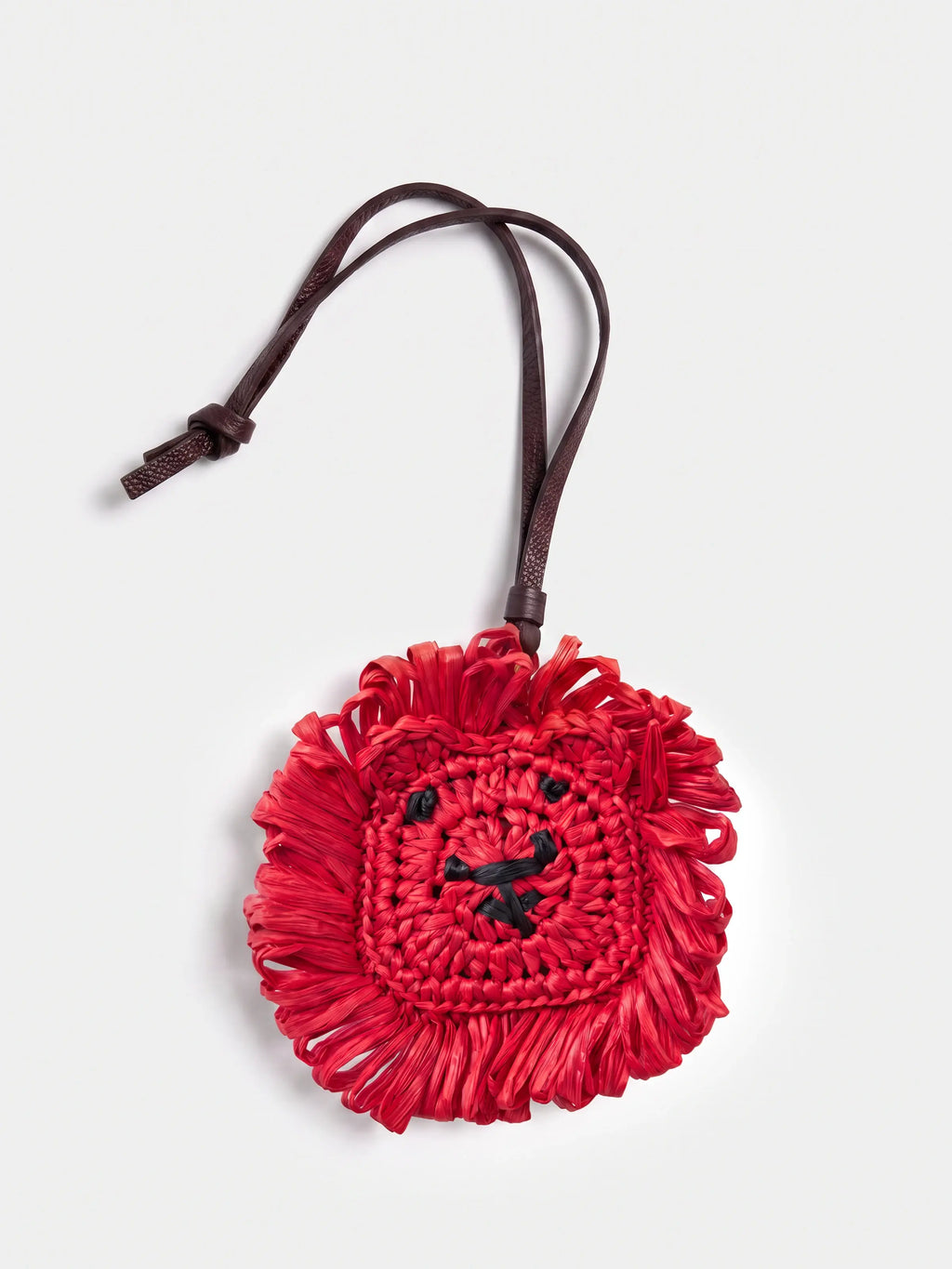 A red fringed woven raffia lion charm with a dark brown strap, photographed on a light gray background.