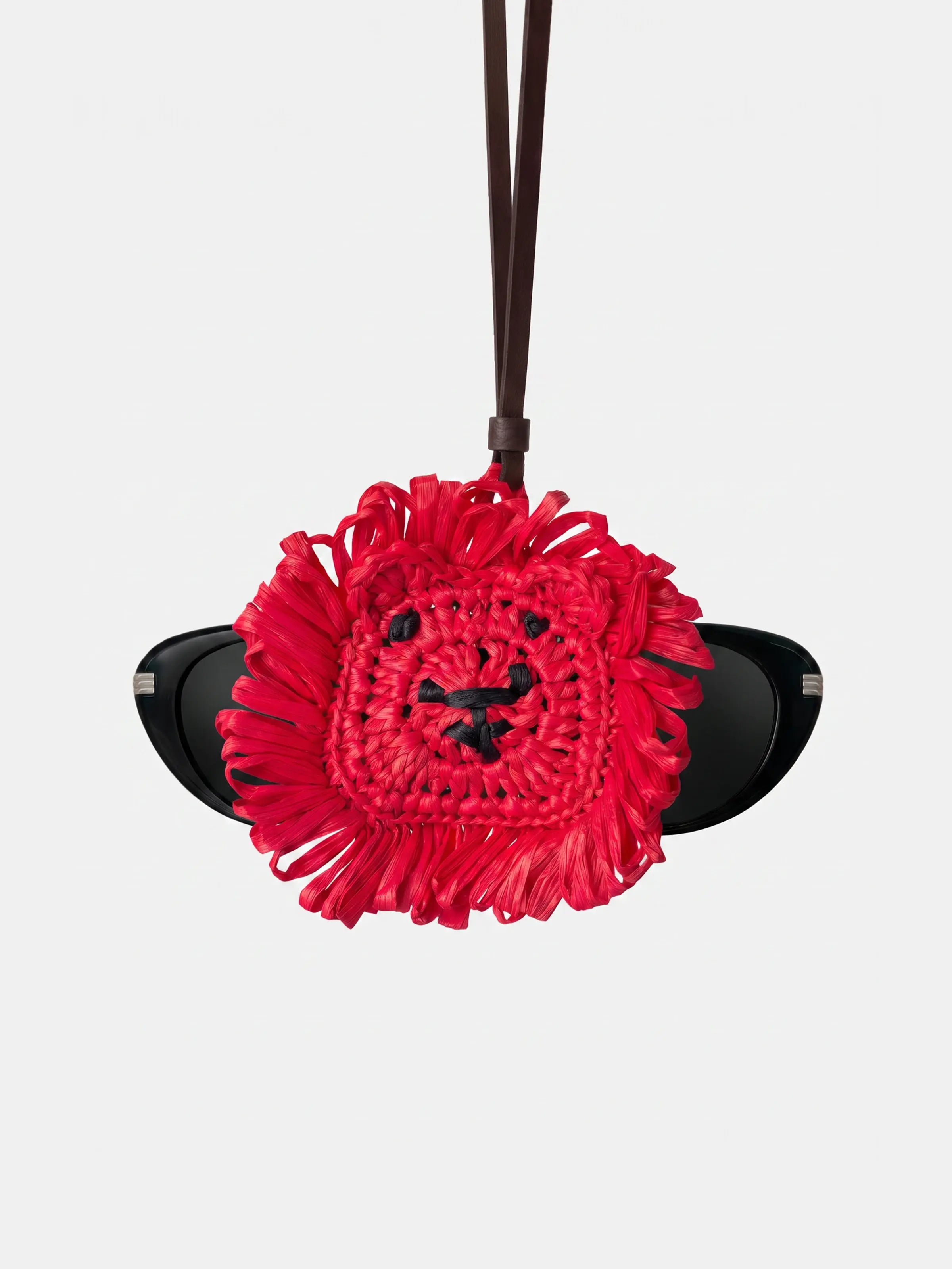 A bright red lion-head sunglasses holder with black leather straps, shown holding a pair of black sunglasses against a light gray background.
