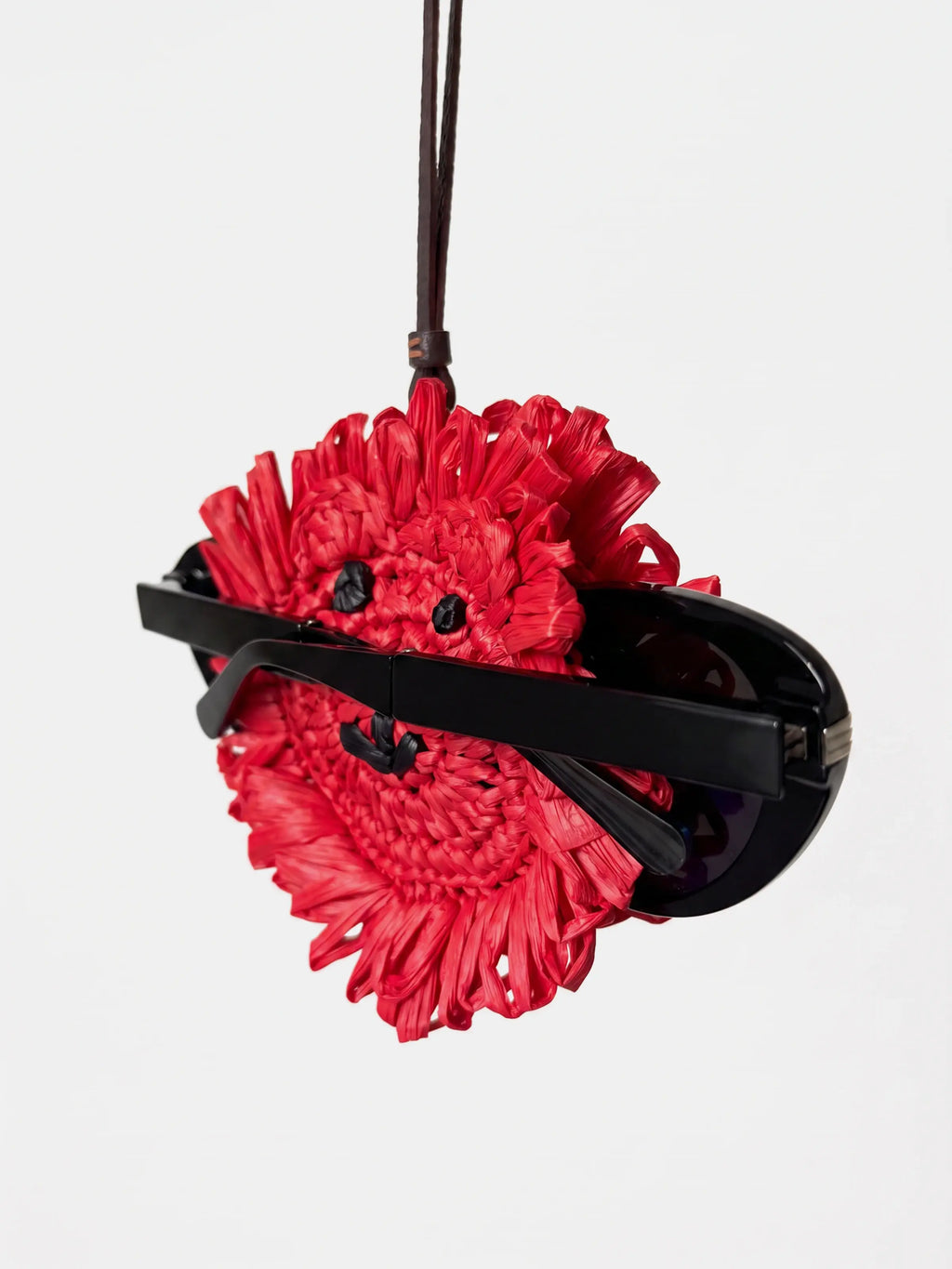A red woven raffia bag with a black leather strap and black sunglasses attached to the front, shown against a plain white background.