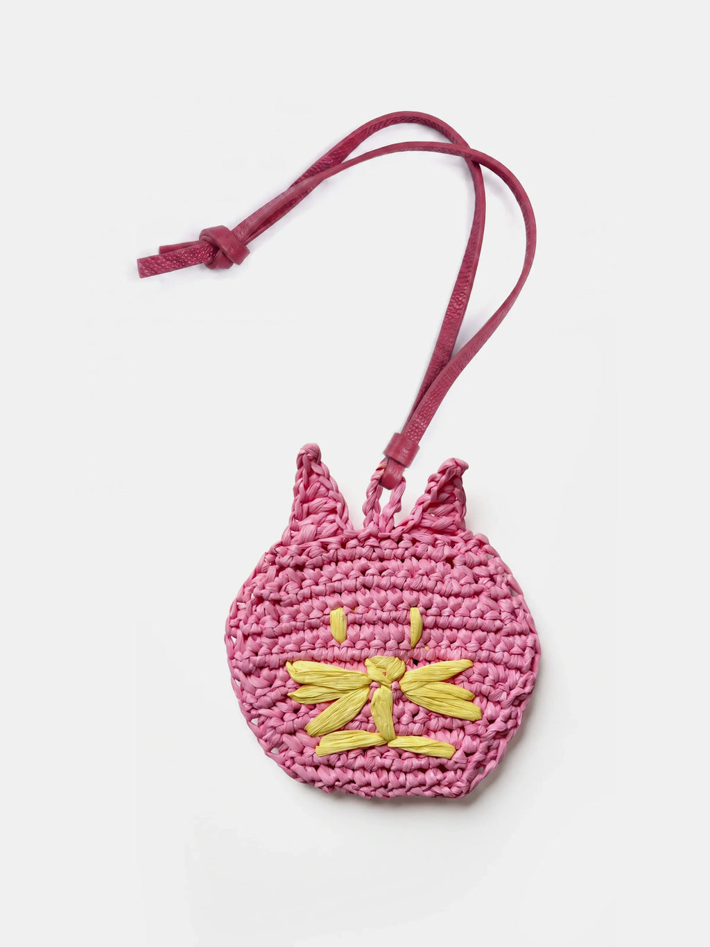 A pink crocheted cat bag charm with a matching pink strap, featuring a yellow embroidered cat face on the front, set against a plain white background.