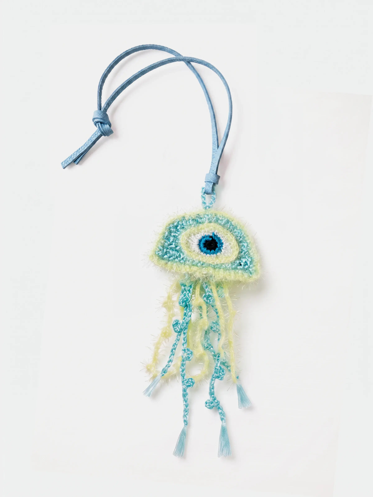 A handmade light blue and mint green jellyfish charm with a knitted eye and dangling tassels, attached to a matching light blue cord, shown on a plain white background.