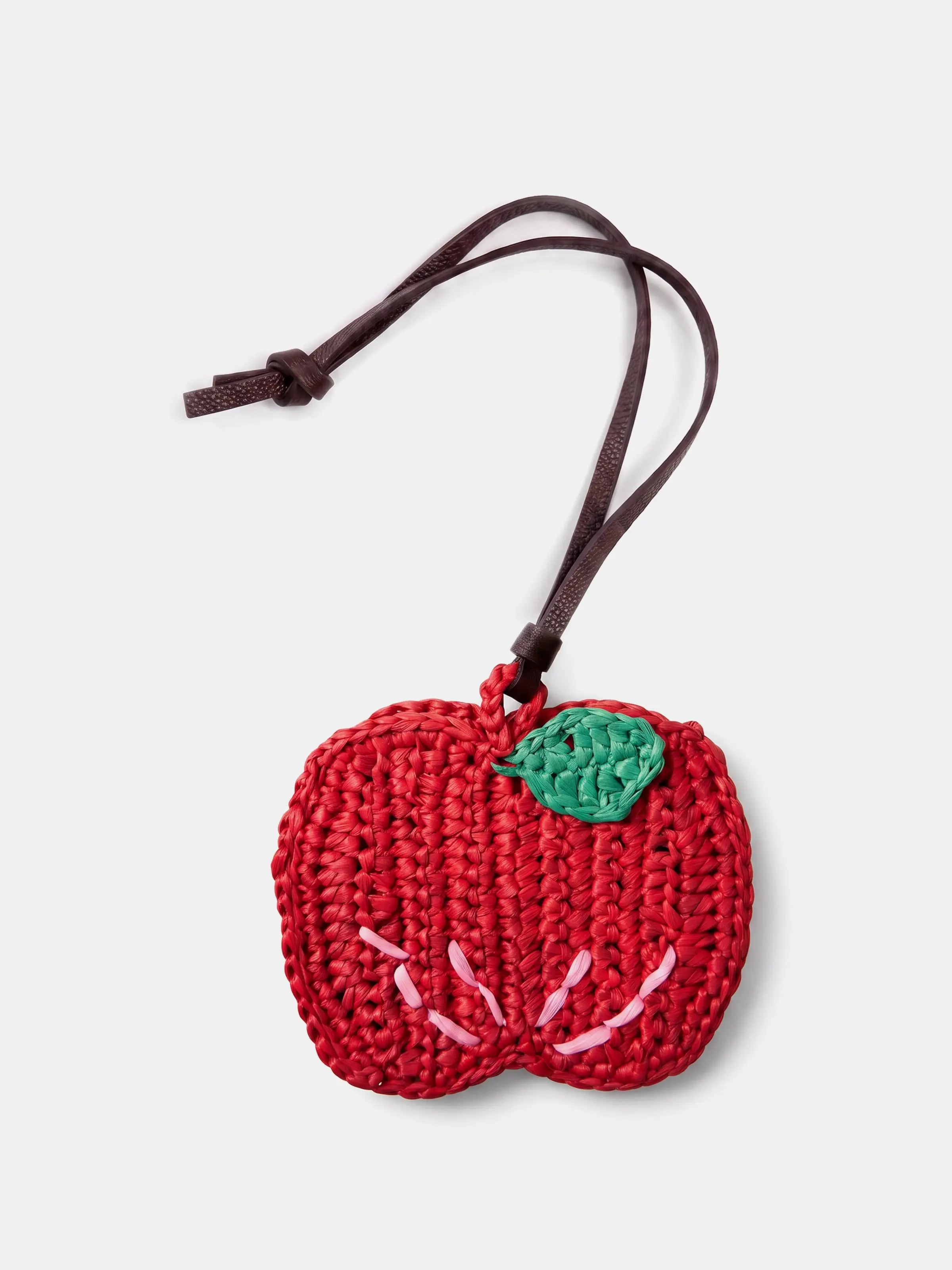 a red apple raffia charm with a brown leather strap