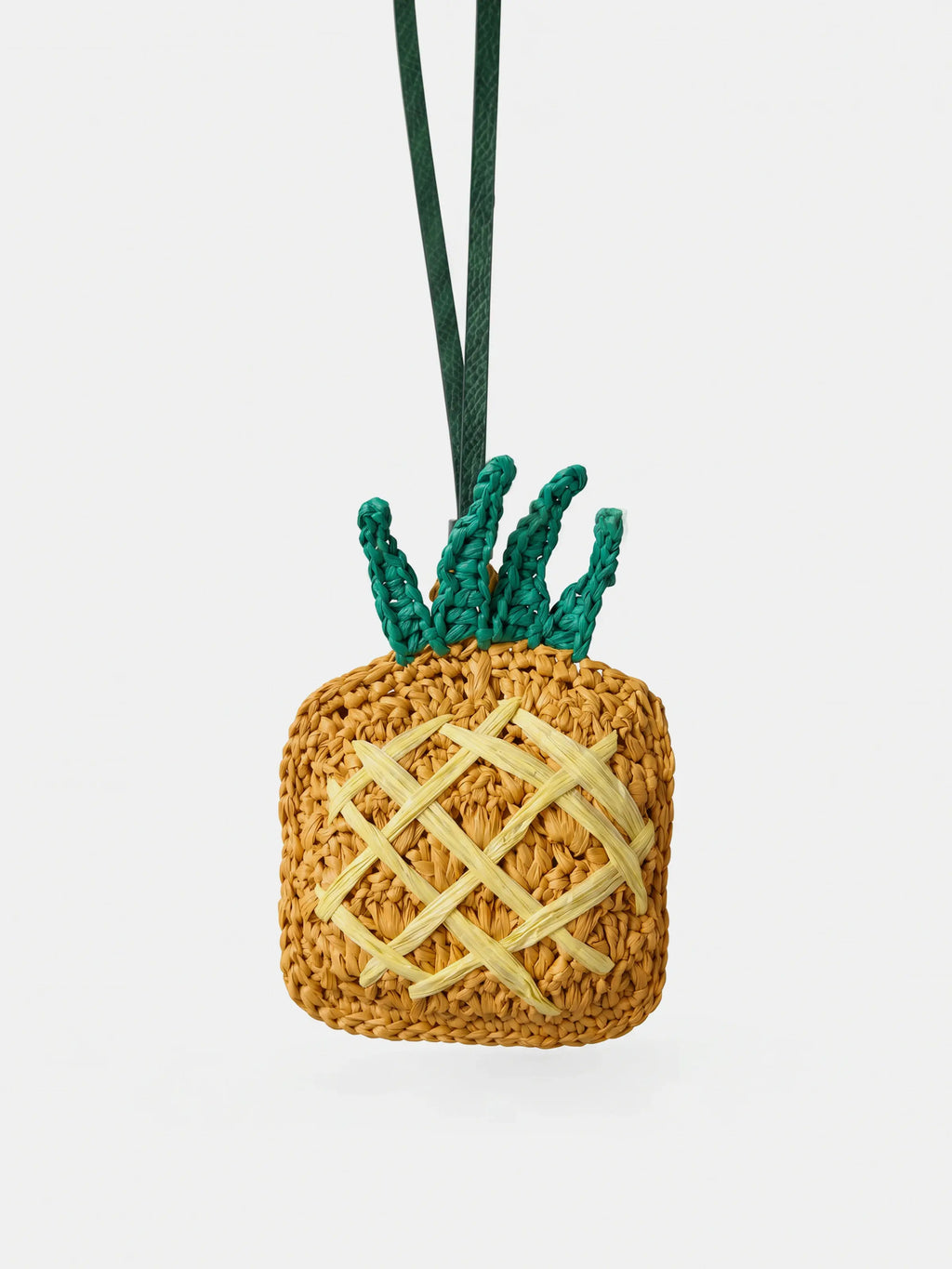 A woven pineapple charm with a natural straw body, green leafy top, and dark green hanging cord, shown on a plain light gray background.