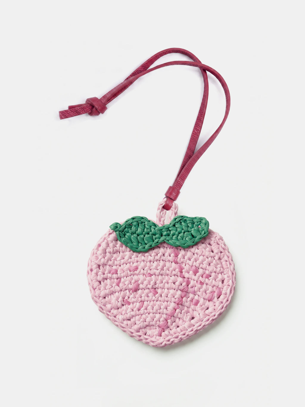 A crocheted peach-shaped raffia charm in light pink with a green leaf detail and a dark pink hanging strap