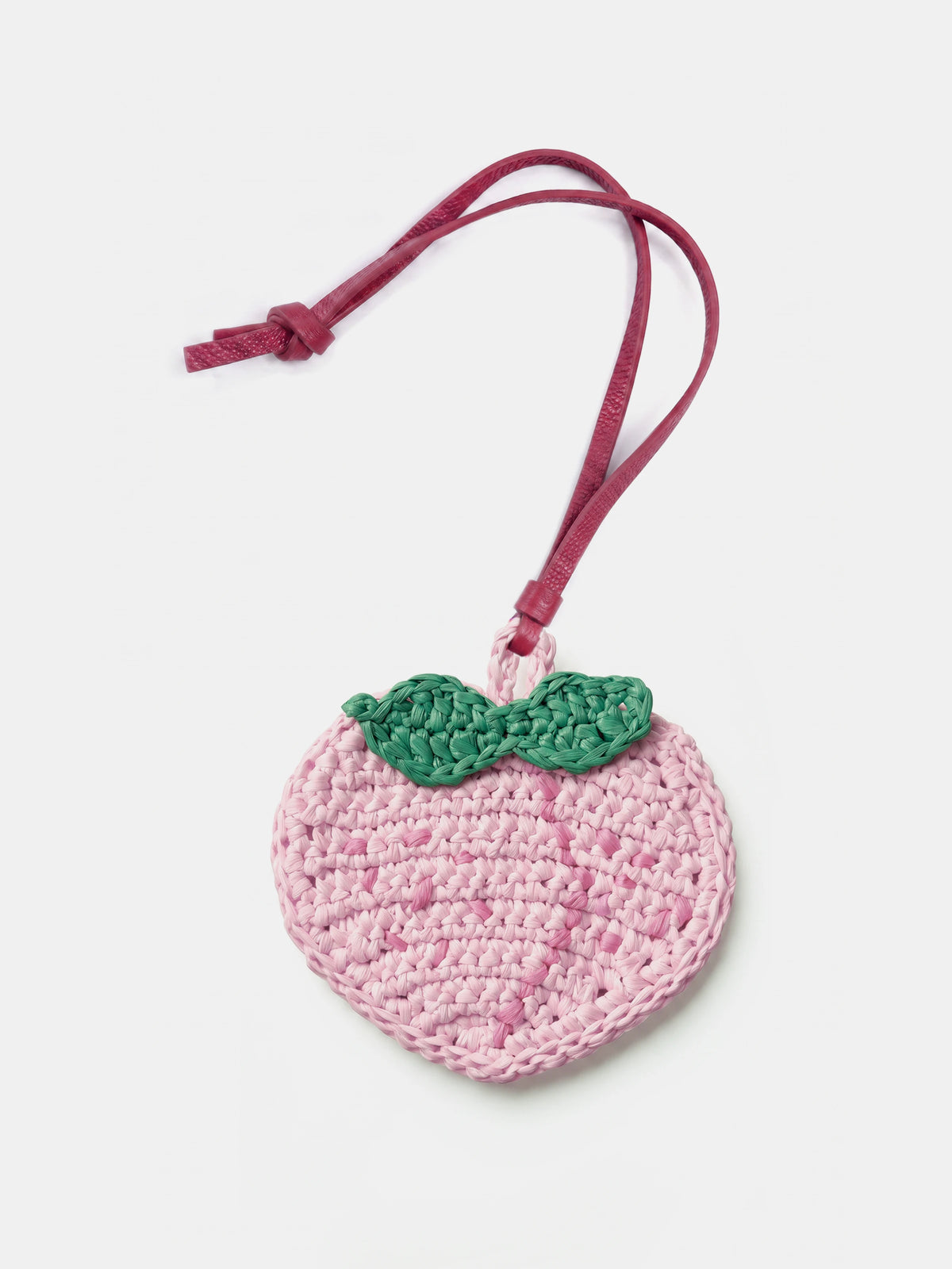 A crocheted peach-shaped raffia charm in light pink with a green leaf detail and a dark pink hanging strap