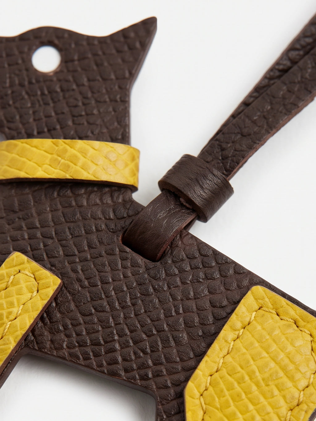 A close-up of a dark brown textured leather accessory with bright yellow contrast panels and strap details, photographed on a clean white background.