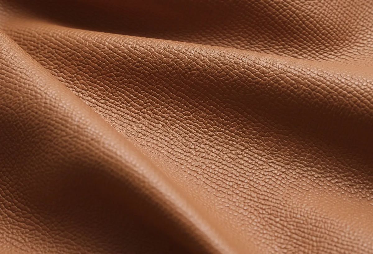 A close-up of draped brown pebbled leather fabric showing its rich texture and fine grain.