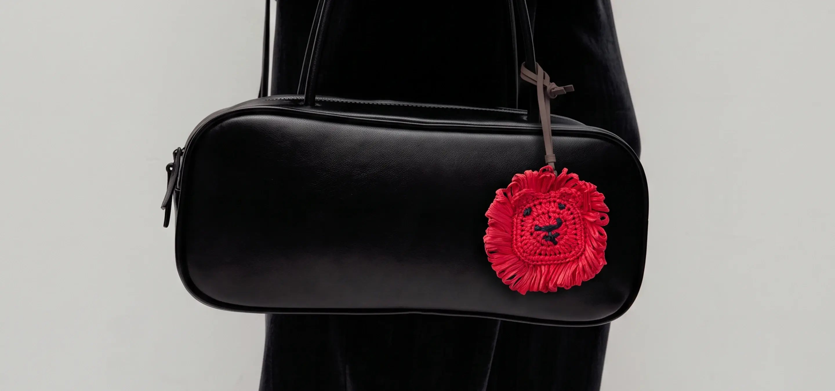 A black leather shoulder bag with a distinctive red lion head charm