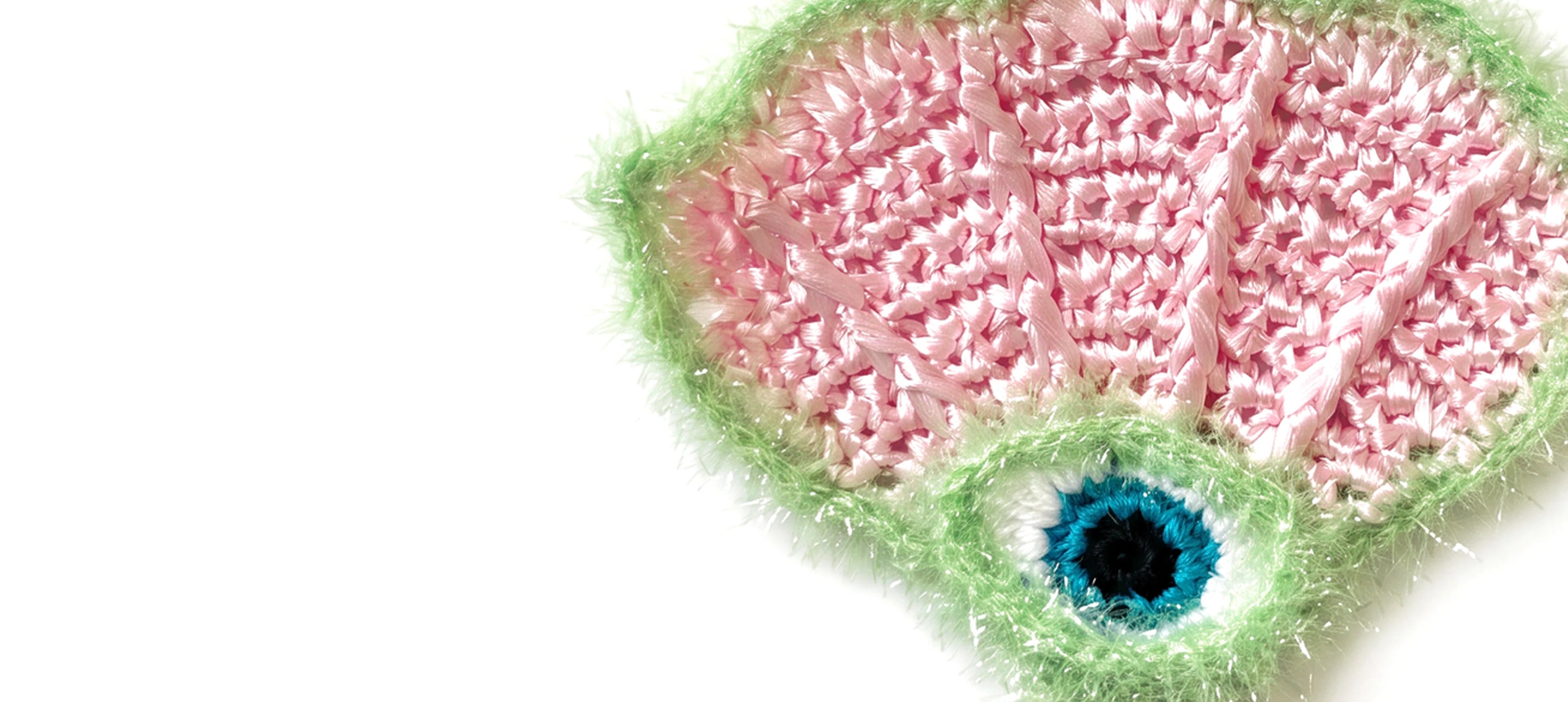A close-up of a crocheted or knitted raffia scallop charm with an evil eye