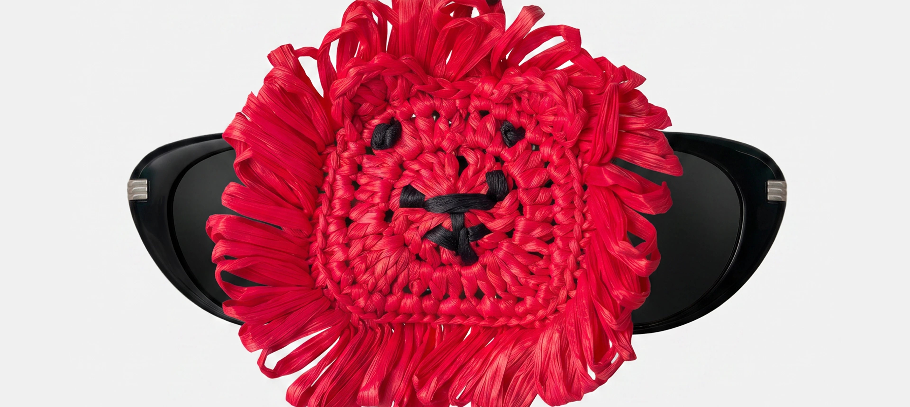 a red woven lion head charm holding a pair of glasses