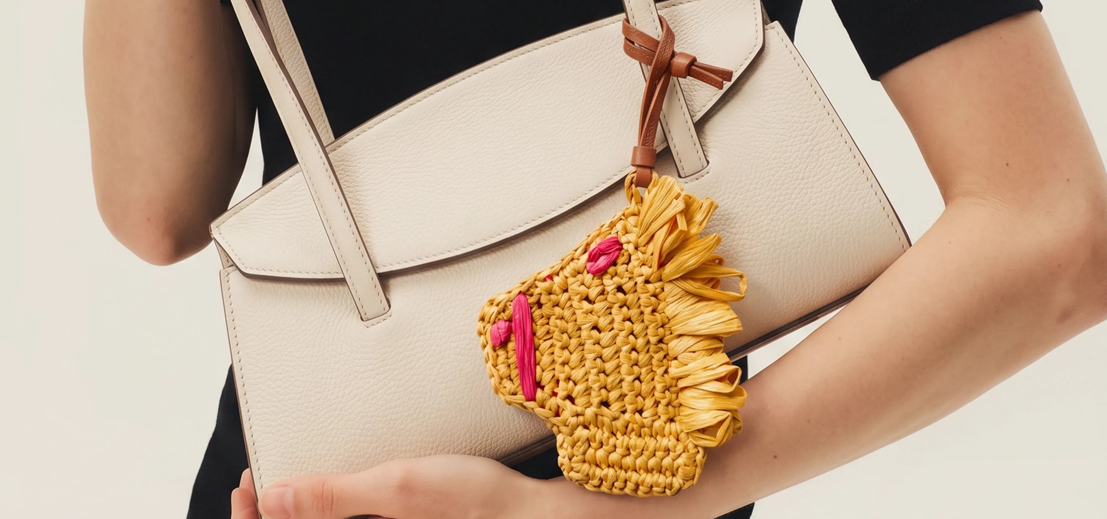 A person carries a black woven tote bag with a yellow raffia horse charm hanging from the handle